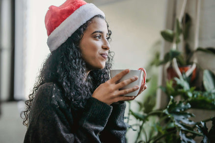 Woman wearing santa hat sipping from mug for holiday self-care
