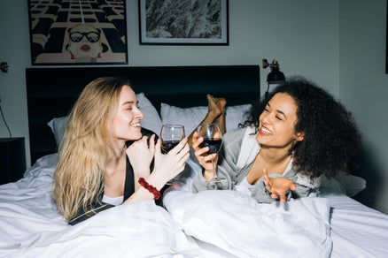 Two women lying in bed with wine for a ladies night in