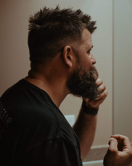 man touching his beard and looking in mirror