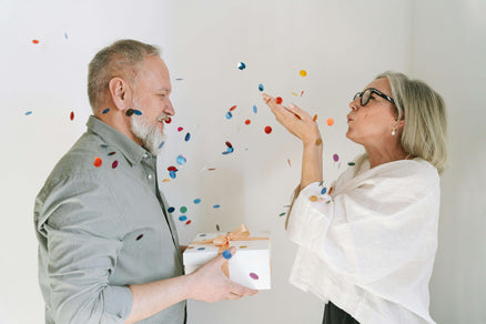 man giving man with beard a gift and blowing confetti