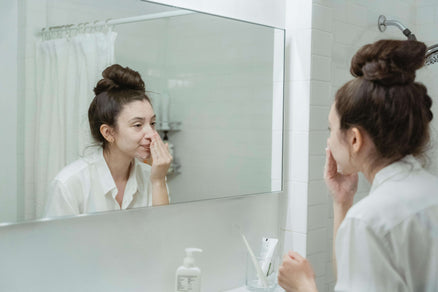 woman looking in mirror and applying skincare