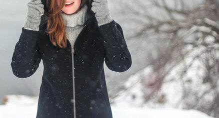 woman with long hair bundled up surrounded by snow in winter